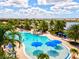 Aerial view of a resort-style pool area with blue umbrellas, lush landscaping, and ample seating at 13511 Esposito St, Venice, FL 34293