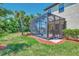 A rear exterior of this home features a screened-in patio that is surrounded by grass and palm trees at 20290 Lagente Cir, Venice, FL 34293