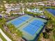 Aerial view of blue tennis courts surrounded by lush landscaping and palm trees in a vibrant community at 5632 Long Shore Loop, Sarasota, FL 34238