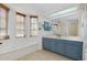 Bathroom with blue vanity, beige floors, and large mirror plus window seat at 610 Alligator Dr, Venice, FL 34293