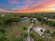 Panoramic aerial shot showcasing the home, pond, and surrounding trees under a vibrant sunset sky at 6824 283Rd E St, Myakka City, FL 34251