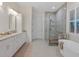 Bright bathroom featuring double vanity, walk-in shower, and soaking tub under shuttered window at 9810 Eagle Preserve Dr, Englewood, FL 34224