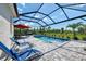 Screened-in pool area with lounge chairs, umbrella-covered table and chairs, and lush green space at 17515 Jadestone Ct, Venice, FL 34293