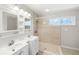 Bathroom with dual sinks, vanity with white cabinets, shower with glass doors, and accent window at 5992 Osprey Rd, Venice, FL 34293
