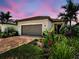 A charming home showcases a brick driveway, a two-car garage, and vibrant tropical landscaping at 13731 Vadini St, Venice, FL 34293