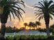 Tranquil Florida landscaping showcasing palm trees with bright sunset, tiered fountain, and white fencing at 4213 Vicenza Dr # A2, Venice, FL 34293