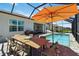 Screened-in pool and spa area with outdoor dining table and chairs, plus an orange sun umbrella at 8529 Saint Kitts Cir, Englewood, FL 34224