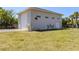 Exterior shot of large garage with three garage doors, surrounded by palms and grass at 13314 Prentice Ave, Port Charlotte, FL 33953