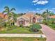 Beautiful single-Gathering home showcasing verdant landscaping, a brick driveway, and a partial view of a lake at 138 Rimini Way, North Venice, FL 34275