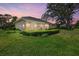 Exterior view of home and screened in patio surrounded by mature trees, lawn, and manicured shrubbery at sunset at 2092 Timucua Trl, Nokomis, FL 34275