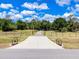 Long concrete driveway leads to a gated property surrounded by lush trees and green pasture at 6293 Taneytown St, North Port, FL 34291