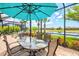 Screened lanai featuring a dining table under an umbrella, with views of the water and lush landscaping at 13873 Karina St, Venice, FL 34293