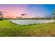 Scenic community pond view featuring lush green lawns, and neighborhood homes in the background at dusk at 2150 Snapdragon Ln, Venice, FL 34292