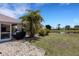Lush backyard with a view of the serene lake, featuring a stone patio and a covered grill area at 25509 Arequipa Dr, Punta Gorda, FL 33983
