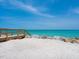 Beach access featuring a wooden walkway leading to white sands and clear, turquoise waters, enhanced with rock barrier at 3516 Casey Key Rd, Nokomis, FL 34275