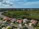 Aerial view of terracotta-roofed home surrounded by similar properties with a green space and blue skies in the background at 4912 Bella Terra Dr, Venice, FL 34293