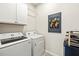 Efficient laundry room with modern appliances, white cabinets, wine storage, and Jazz Fest art at 12538 Somatic Ct, Venice, FL 34293