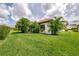Beautifully landscaped backyard featuring lush green lawn, mature palms, and charming home exterior at 241 Marcheno Way, Nokomis, FL 34275