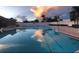 A beautiful pool with lane lines reflects a colorful sunset with palm trees and a white fence at 5966 Willows Bridge Loop, Ellenton, FL 34222