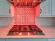 Close-up of a gas range cooktop with a decorative tiled backsplash and a modern vent hood with red lights at 12705 Pinnacle Ln, Venice, FL 34293