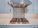 Close up of a gas stovetop with stainless steel vent hood and colorful tile backsplash, set on quartz countertops at 12705 Pinnacle Ln, Venice, FL 34293