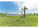 Scenic backyard view overlooking a serene lake with a fountain, framed by swaying palm trees at 12816 Morning Mist Pl, Venice, FL 34293