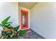 A bright orange front door welcomes you, complemented by lush greenery and a textured white wall at 12816 Morning Mist Pl, Venice, FL 34293
