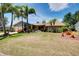 Charming single-story home featuring a lush lawn, mature palm trees, and colorful landscaping under a sunny sky at 915 S Doral Ln, Venice, FL 34293