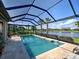 Screened-in pool area featuring travertine tile, lush landscaping, and a beautiful lake view at 13016 Rinella St, Venice, FL 34293