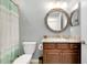 Well-lit bathroom features a decorative round mirror, marble countertop, and wood vanity with a combination shower and tub at 13634 Vancanza Dr, Venice, FL 34293