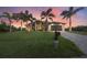 Attractive home with a manicured lawn, palm trees, and a long driveway leading to an attached garage at sunset at 14398 Fort Worth Cir, Port Charlotte, FL 33981