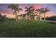 Spacious home with lush lawn, tropical landscaping, and a wide driveway leading to an attached garage at sunset at 14398 Fort Worth Cir, Port Charlotte, FL 33981