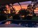 Screened pool with brick patio offers a serene view of the water, framed by a stunning sunset at 249 Hallcrest Ter, Port Charlotte, FL 33954
