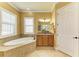 This well-lit main bathroom features a large soaking tub, granite countertops, and ample storage in the wooden cabinets at 20169 Cristoforo Pl, Venice, FL 34293