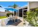 Outdoor patio with a table and chairs under a blue umbrella, surrounded by lush landscaping and a tropical tree at 751 Capri Isles Blvd # 108, Venice, FL 34292