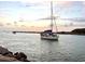 A sailboat navigates through calm ocean waters with a distant crowd on the shore at dusk at 9917 Haze Dr, Venice, FL 34292