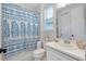 White bathroom with a blue patterned shower curtain, white sink, and window with blinds at 11560 Tapestry Ln, Venice, FL 34293