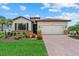 Inviting single-Gathering home showcasing a brick-paved driveway and blooming flowers in the landscape at 11970 Lovegrass St, Venice, FL 34293