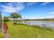 Beautiful lake view from the property, with lush green lawn and colorful landscaping, enhanced by palm trees under a clear blue sky at 2487 Marton Oak Blvd, North Port, FL 34289