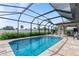 Sparkling blue swimming pool enclosed by a screened lanai with brick pavers and privacy hedges at 7257 Maguire Ln, Englewood, FL 34224