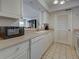 Bright kitchen featuring a microwave, dishwasher, white cabinets, and view into adjacent dining area at 800 Capri Isles Blvd # 235, Venice, FL 34292