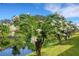 Scenic view of lush landscaping, flowering trees, and tranquil pond reflecting the serene sky at 1100 Capri Isles Blvd # 215, Venice, FL 34292