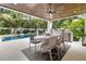 Covered patio with a dining table, outdoor kitchen, and a view of the pool and lush tropical landscaping at 415 N Bay Blvd, Anna Maria, FL 34216