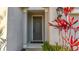 Close up of a front door with a red leafy plant and green fern next to it at 11794 Forest Park Cir, Bradenton, FL 34211