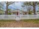 Charming single-story home featuring a red door, a white picket fence, and mature trees in the front yard at 3408 Phillips St, Tampa, FL 33619