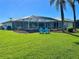 Beautiful backyard features a screened-in patio, lush lawn, palm trees, and inviting Adirondack chairs at 1727 Waxwing Cir, Venice, FL 34293