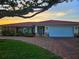 Charming single-story home with a red tile roof, stone accents, and a brick driveway at sunset at 1706 S Lakeside Ct, Venice, FL 34293