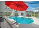 Beautiful pool with outdoor lounge seating, dining set, and a vibrant red umbrella under a screened enclosure at 18526 Sweetbay Ln, Dade City, FL 33523