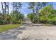 Ranch-style home featuring a gravel driveway lined with mature trees and landscaped greenery at 6559 Tidwell St, North Port, FL 34291