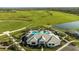 Aerial view of a community clubhouse, pool and parking, set amidst a vast green field and water feature at 6243 Plateau Ct, Bradenton, FL 34203